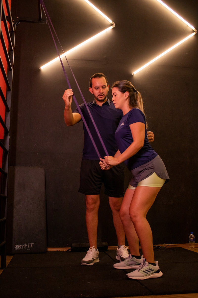 Trainer assisting woman with resistance band exercise.
