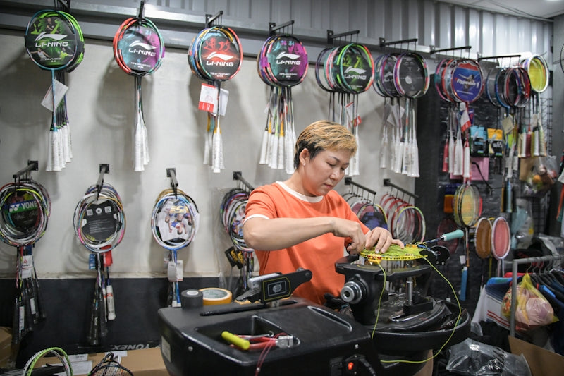 A woman strings a badminton racket in a sports shop.